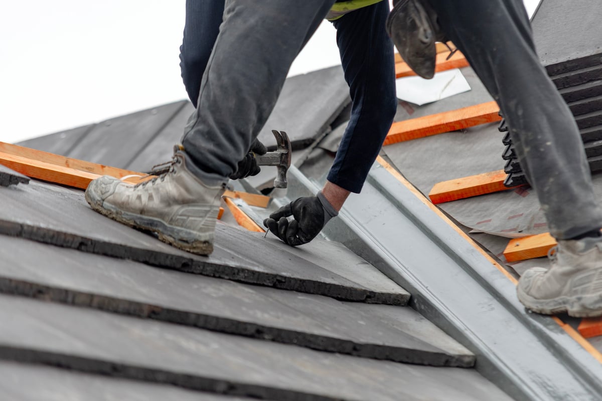 Construction worker carefully places roof tiles on a sloped surface while standing on top of a building showcasing the effort involved in roofing work
