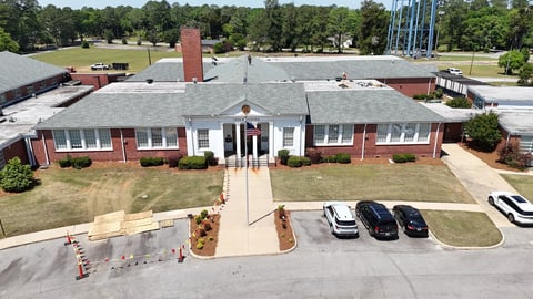 Aerial view of a single-story red brick building with white trim, parking lot, and surrounding trees