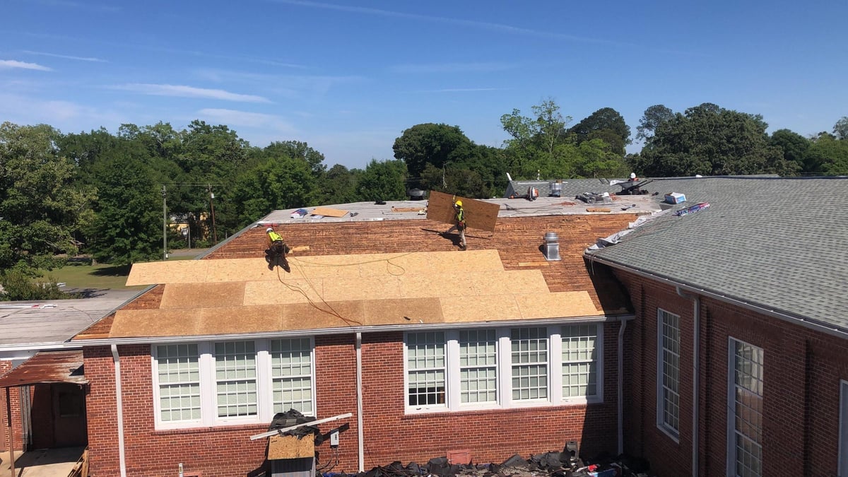 Construction workers on roof of red brick building with plywood covering and partial roof removal visible