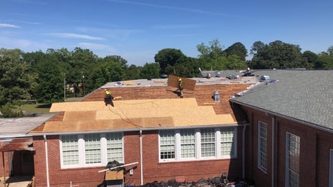 Construction workers on roof of red brick building with plywood covering and partial roof removal visible