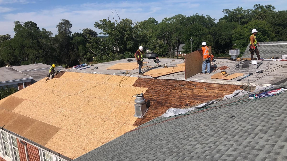Workers installing new roof sheathing and materials on residential home with trees in background